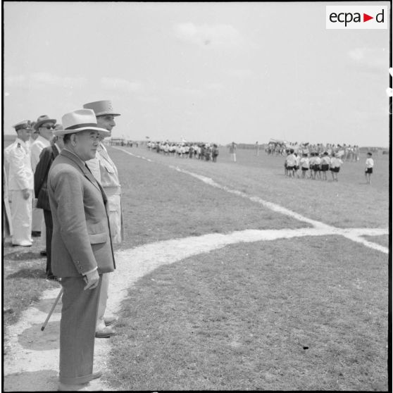 Le général de Lattre de Tassigny, commandant en chef en Indochine et Tran Van Huuu, président du conseil des ministres de l'Etat du Vietnam, assistent au défilé d'enfants vietnamiens au cours d'une cérémonie sur le terrain d'aviation de Vinh Yen.