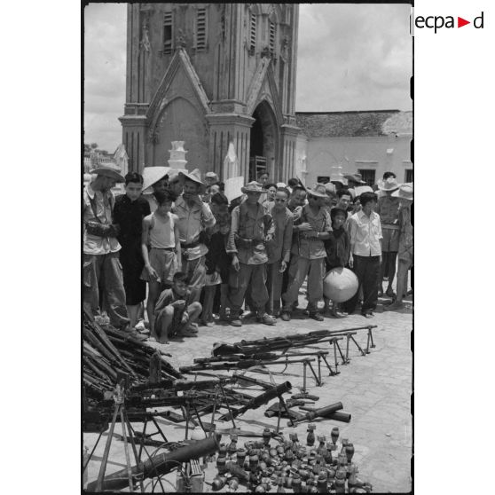 Les armes récupérées à l'ennemi sont exposées en faisceau sur la place de l'église de Ke Sat.