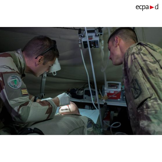 Un médecin des armées du SSA (Service de santé des armées) du Rôle 1 examine la bouche d'un artilleur français de la Task Force Wagram se plaignant de douleurs aux dents, en présence d'un aide soignant américain.