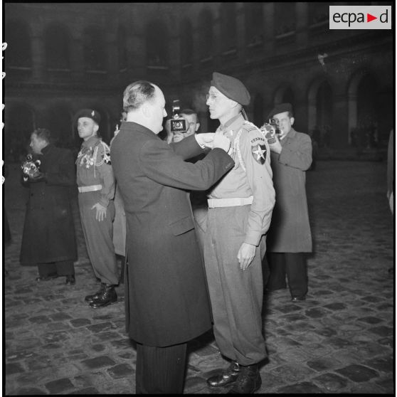 Lors d'une prise d'armes dans la cour d'honneur de l'Hôtel national des Invalides, Pierre de Chevigné, secrétaire d'Etat à la Guerre, remet la croix de la Légion d'honneur au lieutenant Lalager, appartenant au 1er Bataillon Français des Nations Unies (Bataillon de Corée).