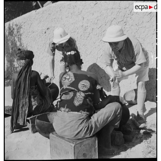 Des officiers des troupes coloniales regardent des femmes qui préparent de l'huile d'arachide.