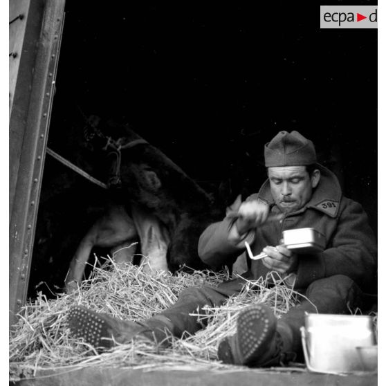 Un soldat mange assis à la porte d'un wagon de marchandises.