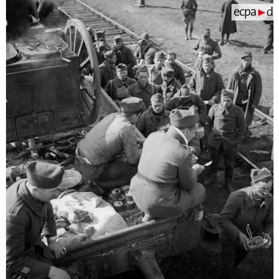 Des soldats perçoivent leur ration pour le repas le long d'une voie ferrée en gare de Trappes.