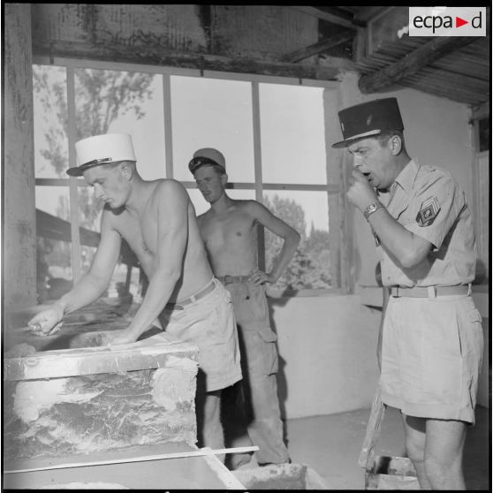 Travaux dans les cuisines du poste du 3e REI (régiment étranger d'infanterie) sous le regard d'un sergent-chef à Arris.