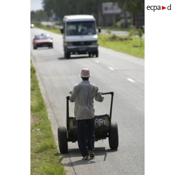 Vie quotidienne à Abidjan. Un homme pousse un chariot artisanal sur le bord d'une route.