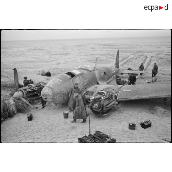 Des civils inspectent les nacelles moteur d'un avion de bombardement Heinkel He-111 du KG-26, endommagé après un atterrissage forcé sur la côte allemande. Ce bombardier Heinkel He 111H 2.KG26 de retour de Scapa-Flow a fait un atterrissage sur une plage à l'ouest de Cuxhaven (20 mars 1940) à  bord, un seul aviateur décède lors de l'atterrisage forcdé, il s'agit de Hans Baehr.