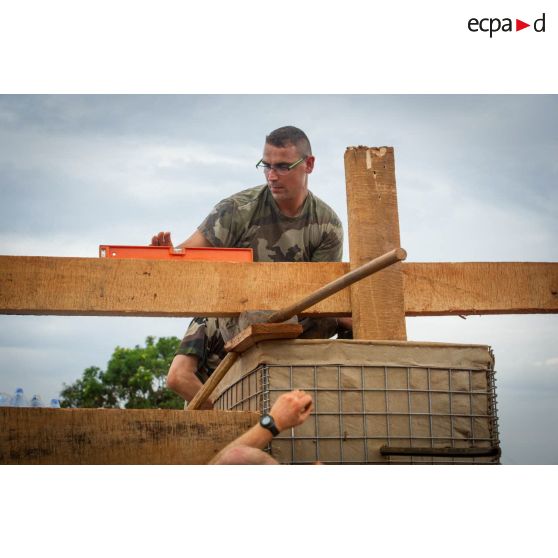 Un soldat du 3e RG mesure la stabilité d'une planche de la charpente d'un bâtiment au moyen d'un niveau à bulle, lors d'une intervention auprès du GTIA (groupement tactique interarmes) Turco, afin de procéder aux réparations des installations de l'aérodrome de Bambari détruites suite au passage d'une tempête.