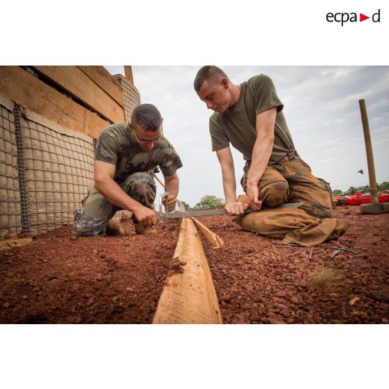 Soldats du 3e RG ajustant une planche de la charpente d'un bâtiment au moyen d'une scie à métaux, lors d'une intervention auprès du GTIA (groupement tactique interarmes) Turco, afin de procéder aux réparations des installations de l'aérodrome de Bambari détruites suite au passage d'une tempête.