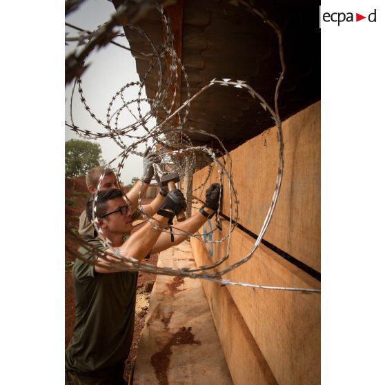 Soldats du 3e RG fixant un réseau de fil barbelé à la charpente d'un bâtiment, lors d'une intervention auprès du GTIA (groupement tactique interarmes) Turco, afin de procéder aux réparations des installations de l'aérodrome de Bambari détruites suite au passage d'une tempête.