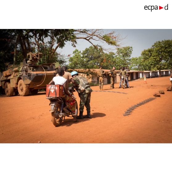 Un casque bleu de la MINUSCA (mission multidimensionnelle intégrée des Nations Unies pour la stabilisation en Centrafrique) contrôle des civils à mobylette, lors d'une mission de contrôle sur un check-point établi sur l'axe du marché central de Bambari, en compagnie des tirailleurs de la compagnie Rouge du 1er RT du GTIA (groupement tactique interarmes) Turco.