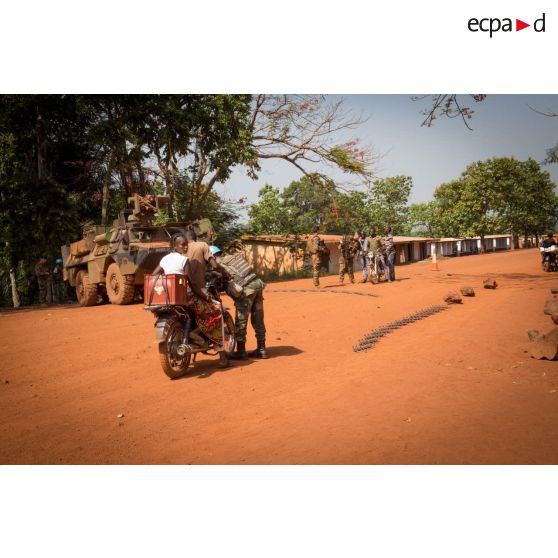 Un casque bleu de la MINUSCA (mission multidimensionnelle intégrée des Nations Unies pour la stabilisation en Centrafrique) contrôle des civils à mobylette, lors d'une mission de contrôle sur un check-point établi sur l'axe du marché central de Bambari, en compagnie des tirailleurs de la compagnie Rouge du 1er RT du GTIA (groupement tactique interarmes) Turco.