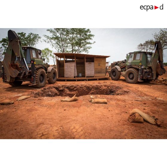 Deux tractopelles EGRAP (engin du génie rapide de protection) conduites par les soldats du groupe d'appui du Génie du GTIA (groupement tactique interarmes) Turco s'apprêtent à soulever un module sanitaire afin de le transporter d'une fosse septique à une autre, dans le cadre du réaménagement des installations sanitaires de la POD (plateforme opérationnelle défense) de Bambari.