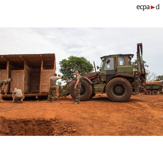 Une tractopelle EGRAP (engin du génie rapide de protection), conduite par les soldats du groupe d'appui du Génie du GTIA (groupement tactique interarmes) Turco, soulève un module sanitaire afin de le transporter d'une fosse septique à une autre, dans le cadre du réaménagement des installations sanitaires de la POD (plateforme opérationnelle défense) de Bambari.