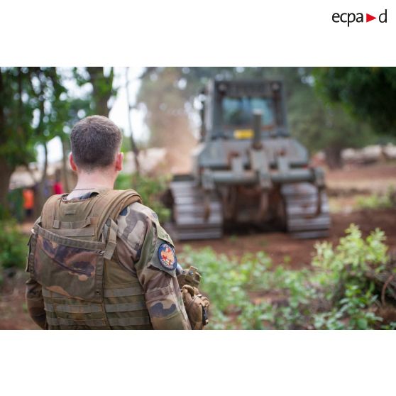 Sous les yeux d'un soldat, un bulldozer Liebherr de type PR 724 LGP du 25e RGA déboise une zone en prévision de la réalisation d'un terrain de football au profit des habitants du village de Makangé.