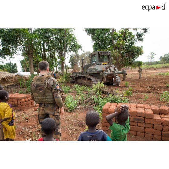 Sous les yeux d'un soldat et d'enfants des environs, un bulldozer Liebherr de type PR 724 LGP du 25e RGA déboise une zone en prévision de la réalisation d'un terrain de football au profit des habitants du village de Makangé.