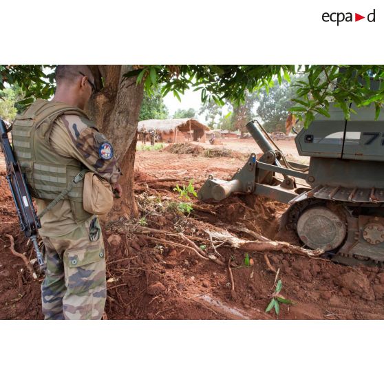 Sous les yeux d'un soldat, un bulldozer Liebherr de type PR 724 LGP du 25e RGA déboise une zone en prévision de la réalisation d'un terrain de football au profit des habitants du village de Makangé.