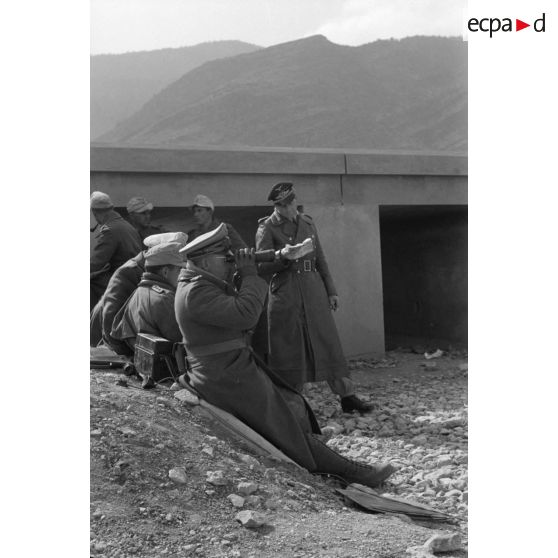 Le général (Generalleutnant) Bülowius, assis près d'un téléphone de campagne, observe le terrain à la jumelle.