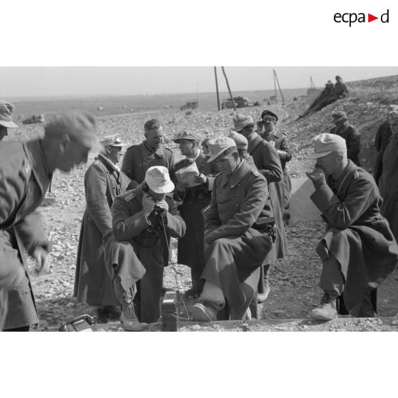 Un groupe d'officiers entoure un téléphone de campagne, à gauche, au second plan, le colonel (Oberst) Fritz Bayerlein.