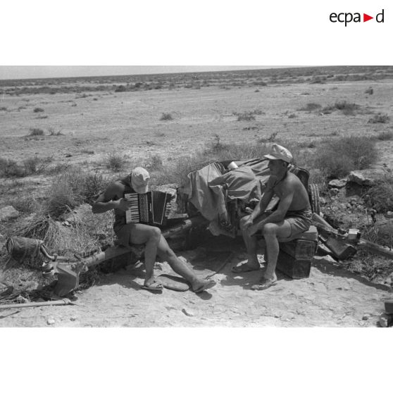 Un soldat joue de l'accordéon sur une flèche d'un canon antichar 5 cm PaK 38, sous le regard d'un camarade.