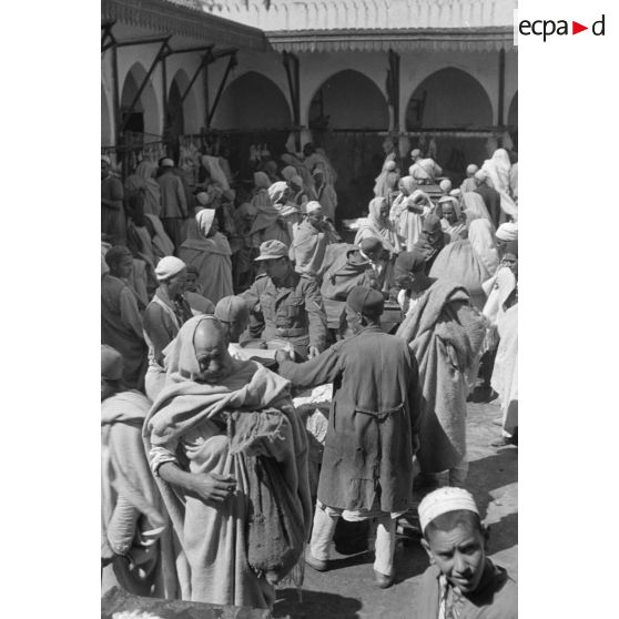 A Tripoli, un caporal allemand circule dans les allées d'un marché, rentre en contact avec les marchands.