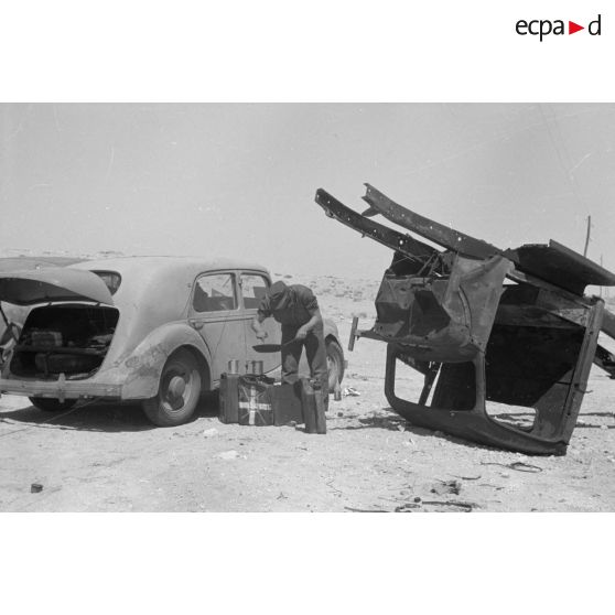 Des hommes du 155e Panzer Artillerie Regiment (Pz.Art.Rgt-155) cuisinent et changent une roue de leur véhicule tandis que des camions passent sur la route