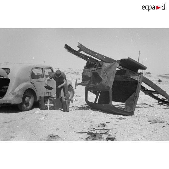 Des hommes du 155e Panzer Artillerie Regiment (Pz.Art.Rgt-155) cuisinent et changent une roue de leur véhicule tandis que des camions passent sur la route