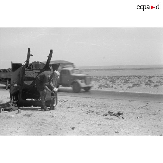 Des hommes du 155e Panzer Artillerie Regiment (Pz.Art.Rgt-155) cuisinent et changent une roue de leur véhicule tandis que des camions passent sur la route