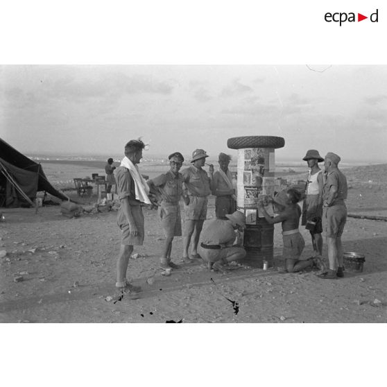 Une colonne de fortune est utilisée par des soldats allemands pour y coller des photographies tirées de magazines.