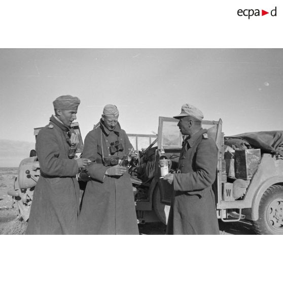 Trois officiers viennent de trouver des bouteilles dans un véhicule britannique, au centre le reporter Hermann Dressler (caméraman et photographe)