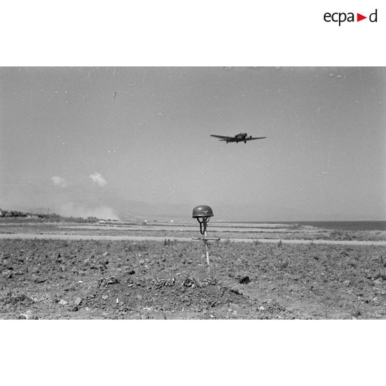 La tombe d'un parachutiste allemand à proximité du terrain de Rethymnon, un avion de transport Junkers Ju-52 s'apprête à atterrir.