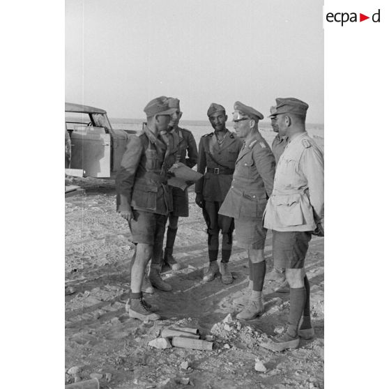 Les généraux Rommel et Gause en conversation avec un lieutenant (Leutnant), peut-être un interprète, entourés d'officiers allemands et italiens.