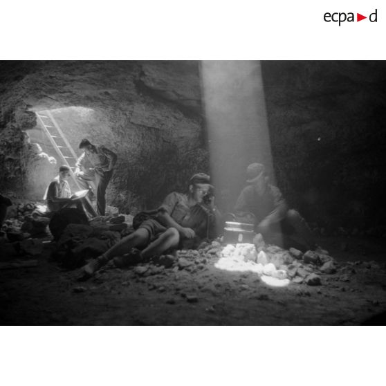 Deux soldats utilisent un téléphone de campagne à l'intérieur d'une grotte où filtre un rayon de lumière.