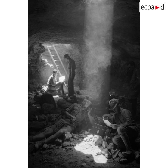 Deux soldats utilisent un téléphone de campagne dans la grotte sous un rayon de lumière. L'un d'eux fume.