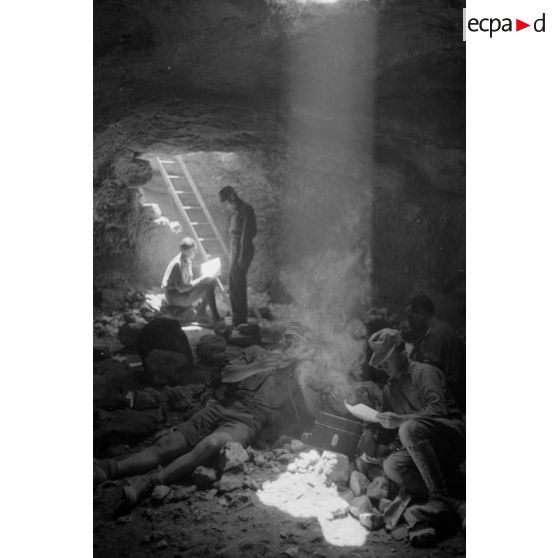 Deux soldats utilisent un téléphone de campagne dans la grotte sous un rayon de lumière. L'un d'eux fume.