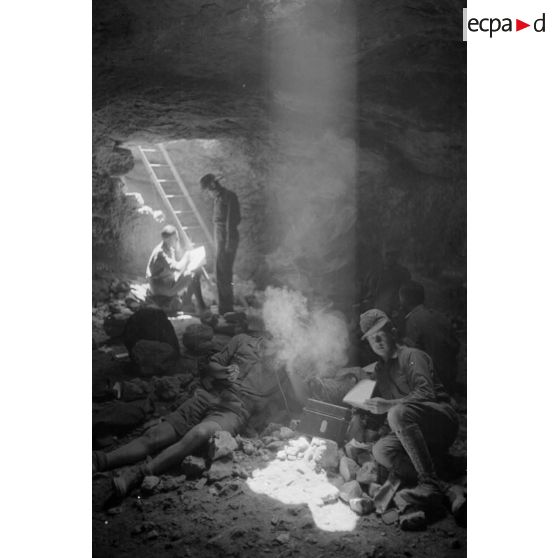 Deux soldats utilisent un téléphone de campagne dans la grotte sous un rayon de lumière. L'un d'eux fume.