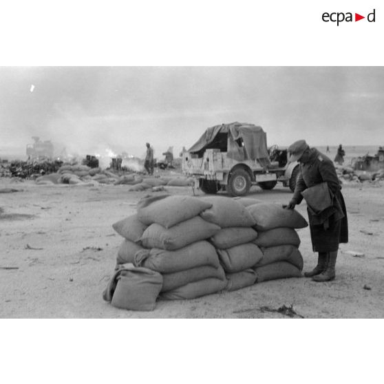 Un soldat allemand lit le texte imprimé sur des sacs capturés après le départ des forces britanniques.