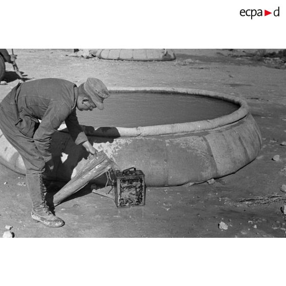 Un soldat remplit une nourrice d'eau. Cette eau a été recueillie dans un bac souple circulaire.