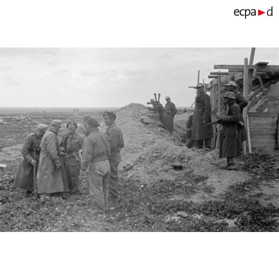 Près du parapet et d'une construction en planches, un officier allemand interroge des prisonniers britanniques.