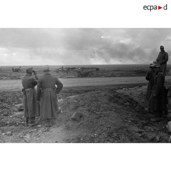 Un groupe de soldats et d'officiers observe les combats derrière une unité de canons légers en batterie.