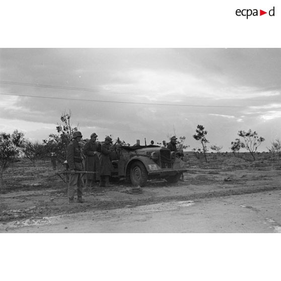 Une voiture Horch Kfz-16 garée au bord de la via Balbia, au milieu d'arbustes rachitiques, est entourée de soldats.