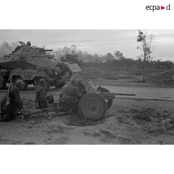 Des soldats sont accroupis près de la route derrière un canon de 3,7 cm PaK en batterie.