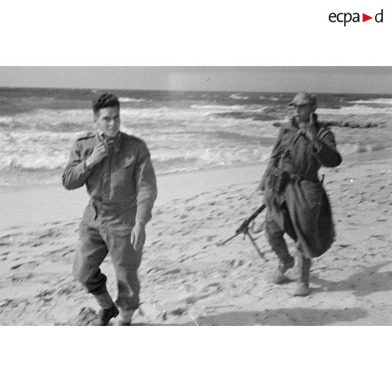 Un soldat allemand tenant une mitrailleuse MG-34 conduit un prisonnier britannique le long d'une plage.