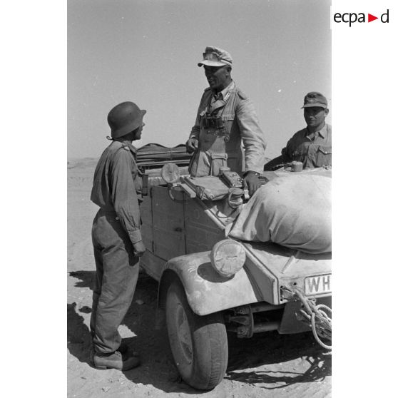 Le colonel (Oberst) Alfred Bruer commandant du Panzer-Artillerie-Regiment 155 de la 21. Panzer-Division, debout dans une voiture Kübelwagen, parle avec ses officiers.