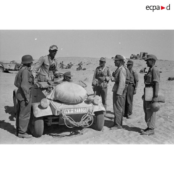 Le colonel (Oberst) Alfred Bruer commandant du Panzer-Artillerie-Regiment 155 de la 21. Panzer-Division, debout dans une voiture Kübelwagen, parle avec ses officiers.