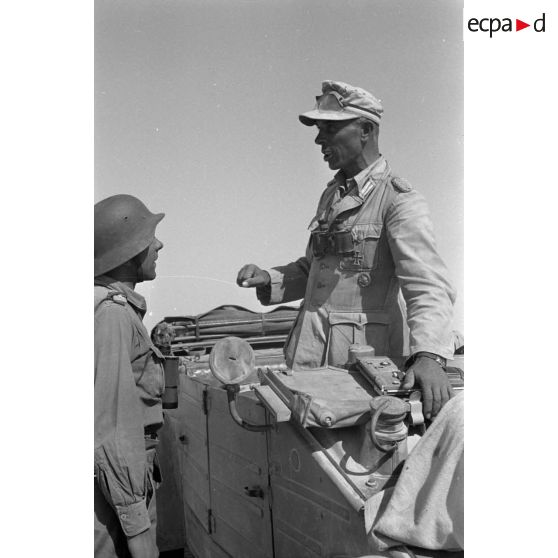 Le colonel (Oberst) Alfred Bruer commandant du Panzer-Artillerie-Regiment 155 de la 21. Panzer-Division, debout dans une voiture Kübelwagen, parle avec ses officiers.