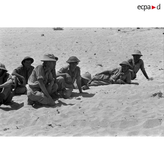 Des prisonniers britanniques accroupis et allongés dans le sable.