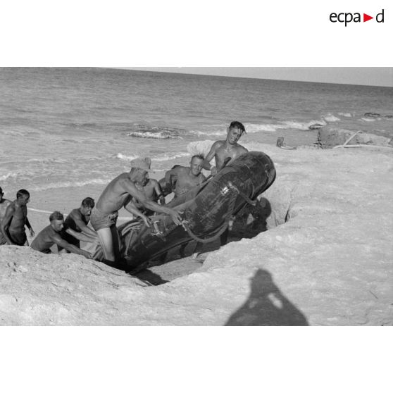 Après avoir déposé un tuyau pour pomper l'eau de mer, des soldats tirent un canot pneumatique sur la plage.