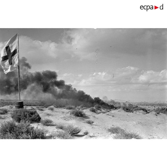 Des débris d'un avion en feu près d'un drapeau de la croix rouge dans le désert.