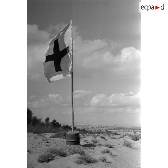 Des débris d'un avion en feu près d'un drapeau de la croix rouge dans le désert.