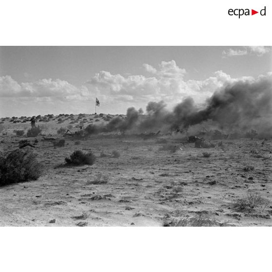 Des débris d'un avion en feu près d'un drapeau de la croix rouge dans le désert.